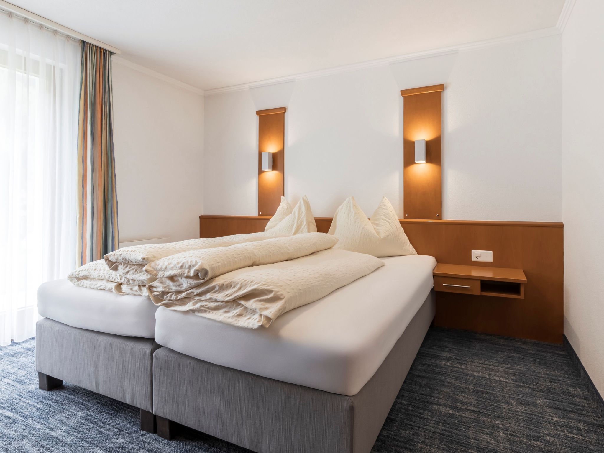 Habitació d'hotel amb un llit, taules de nit i una finestra amb cortines.