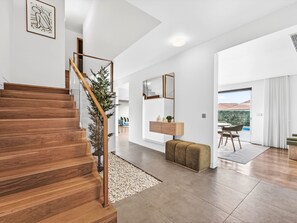 A modern interior with a wooden staircase, a living area with a sofa and a coffee table, a dining area with chairs, and a view through a glass door. - Al Mirase by Interhome (Funchal (Madeira))