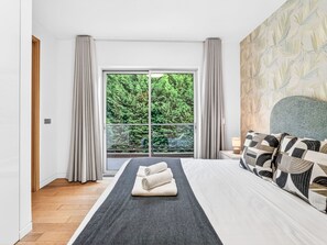 A modern bedroom with a large bed, a view of greenery through a sliding door, and a patterned wall. - Al Mirase by Interhome (Funchal (Madeira))