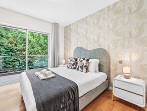 A modern bedroom with a large window, a bed with a headboard, bedside tables, and a nightstand. - Al Mirase by Interhome (Funchal (Madeira))