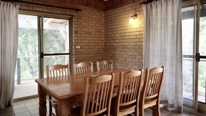 Uma mesa de jantar de madeira com seis cadeiras, uma parede de tijolos e uma porta de vidro deslizante com cortinas.