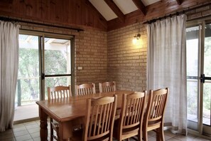 A wooden dining table with six chairs, a brick wall, and a sliding glass door with curtains. - Riverscape Cottage No.12 with river views - Riverscape  - unit 12 with river views (Augusta)