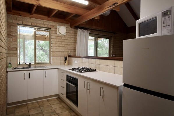 A compact kitchen with white cabinets, a gas stove, a built-in oven, and a refrigerator.