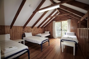 Ein Schlafsaalzimmer mit drei Etagenbetten, Holzwänden und einer schrägen Decke mit freiliegenden Balken.