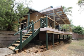Eine Holztreppe führt zu einer Terrasse mit Metallgeländer, umgeben von einem Garten und Bäumen.