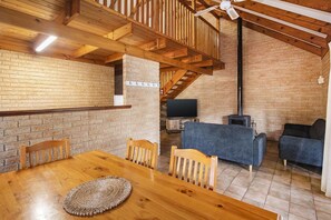 A cozy living room with a wooden dining table, blue sofas, and a brick wall. - Riverscape Cottage No.11 - Riverscape - unit 11 with views over the Blackwood River and fire place (Augusta)