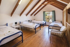 Ein Schlafsaalzimmer mit vier Betten, Holzdielen und einer schrägen Decke mit freiliegenden Balken.