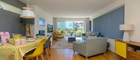 A modern living room with a dining area, a sofa, a yellow cabinet, and a view of the outside.