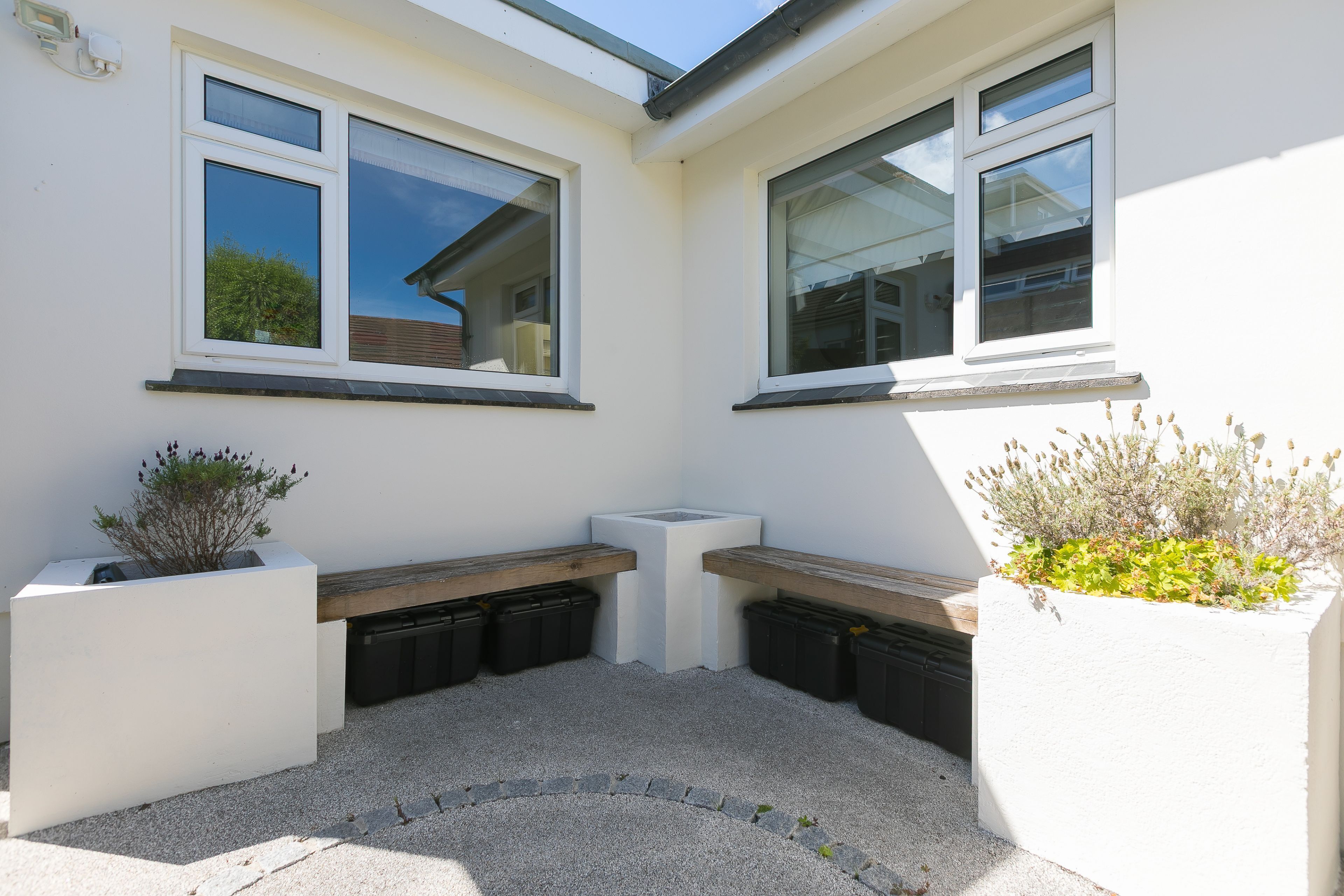 A corner of a building with two windows, a bench, and planters.