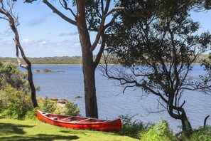 A red canoe on grass near a lake with trees and a clear sky.
