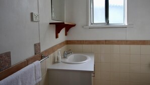 Un baño con lavamanos blanco, espejo, toallero y ventana.
