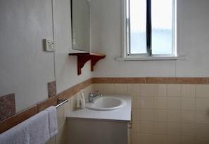 Un baño con lavamanos blanco, espejo, toallero y ventana.