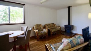 Una sala de estar con una mesa redonda de madera, dos sillones, un sofá, un televisor y una chimenea.