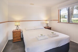 A hotel room with a bed, two bedside tables with lamps, a window with a view, and a wooden headboard. - Riverscape Cottage No.4 - Riverscape Cottage No.4 is an easy walk to the Blackwood River (Augusta)