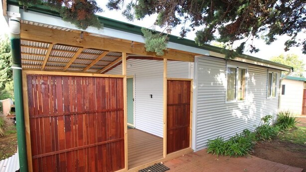 Una casa de un piso con un porche cubierto, un patio trasero cercado y un pequeño jardín delantero.