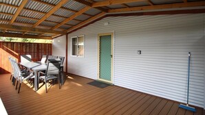Un patio techado con piso de madera, una mesa y sillas, y una puerta con mosquitero.