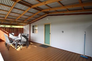 A covered patio with a wooden deck, a table and chairs, and a door with a mesh screen. - Riverscape Cottage No.5 - Riverscape - unit 5 (Augusta)