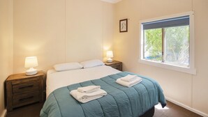 A bedroom with a bed, two bedside lamps, a window with a view, and a small bedside table. - Riverscape Cottage No.8 with River Views - Riverscape - unit 8 with views over the Blackwood River (Augusta)
