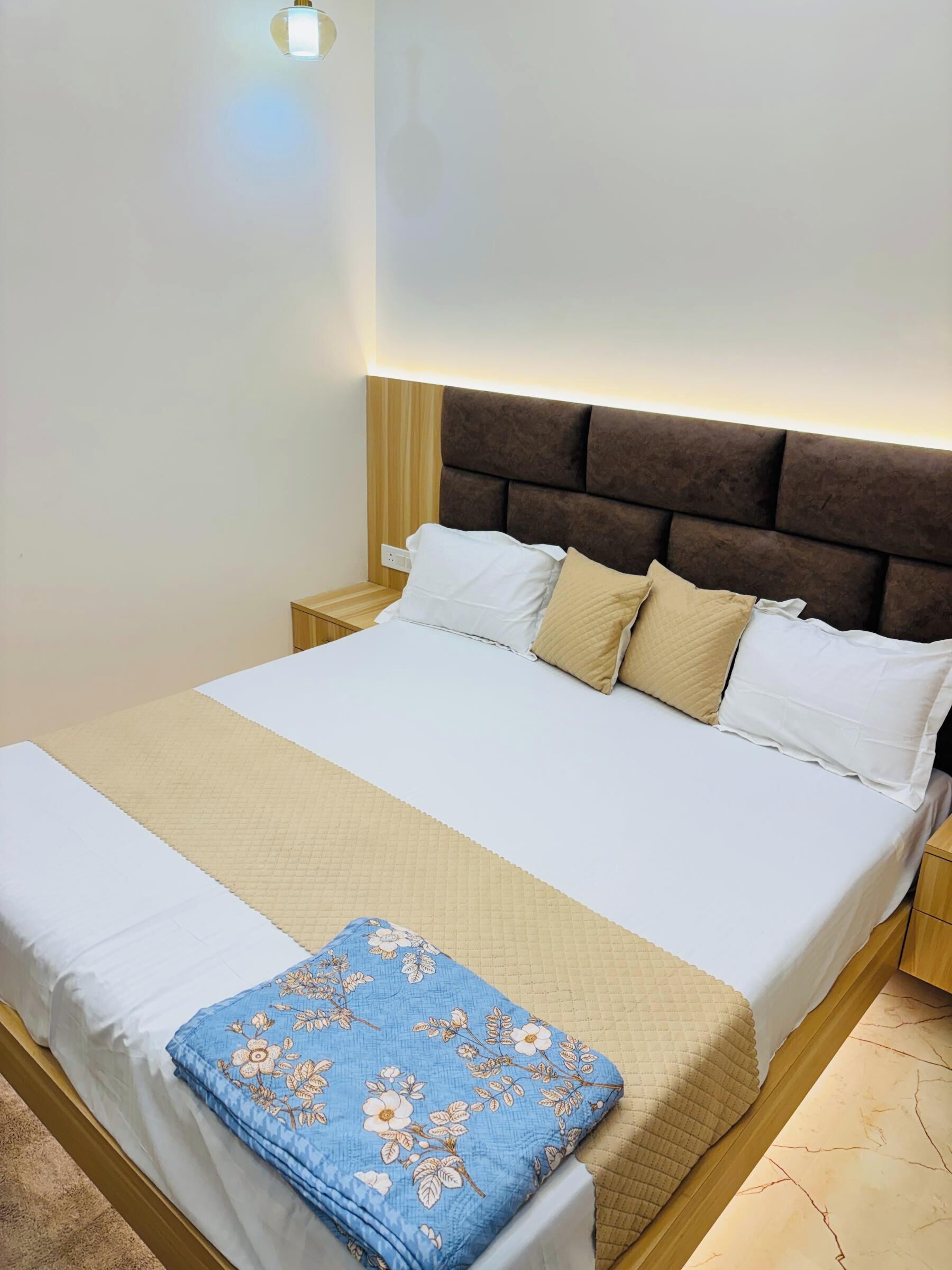 A neatly made bed with a headboard, a bedside table, and a wall-mounted light.