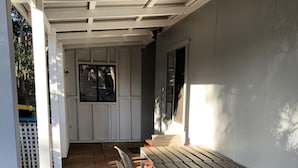 Een terras buiten met een lange tafel en stoelen, een overdekt gedeelte met een afdak en een witte hek.