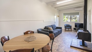 Een eetgedeelte met een ronde houten tafel en stoelen, een bank, een televisie en een open haard.