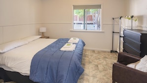 Een slaapkamer met een bed, een raam, een dressoir en een stoel.