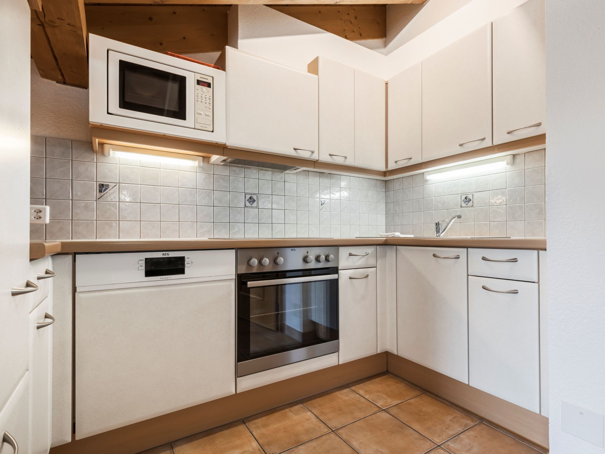Cozinha com armários brancos, forno embutido, micro-ondas e painel de azulejos.