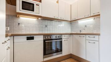 Cozinha com armários brancos, forno embutido, micro-ondas e painel de azulejos.