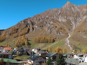 Un pueblo de montaña con edificios tradicionales, una carretera sinuosa y una imponente montaña al fondo.
