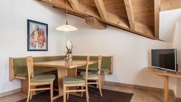 Un coin repas avec une table et des chaises en bois, un tableau accroché au mur et un téléviseur posé sur un meuble.