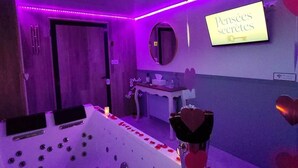 Habitación con una bañera grande, un espejo, un letrero que dice 'Pensées secrètes' y adornos con forma de corazón.