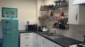 A compact kitchen with a teal refrigerator, white cabinets, a gas stove, and a skylight. - Super Comfy, Convenient two Bedroom Apartment (Corsham)