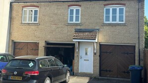 A two-story house with a garage, a white door, and two windows. - Super Comfy, Convenient two Bedroom Apartment (Corsham)