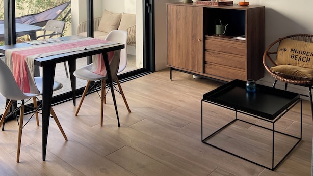 A modern living room with a dining area, a wooden cabinet, a wicker chair, and a hanging light fixture.