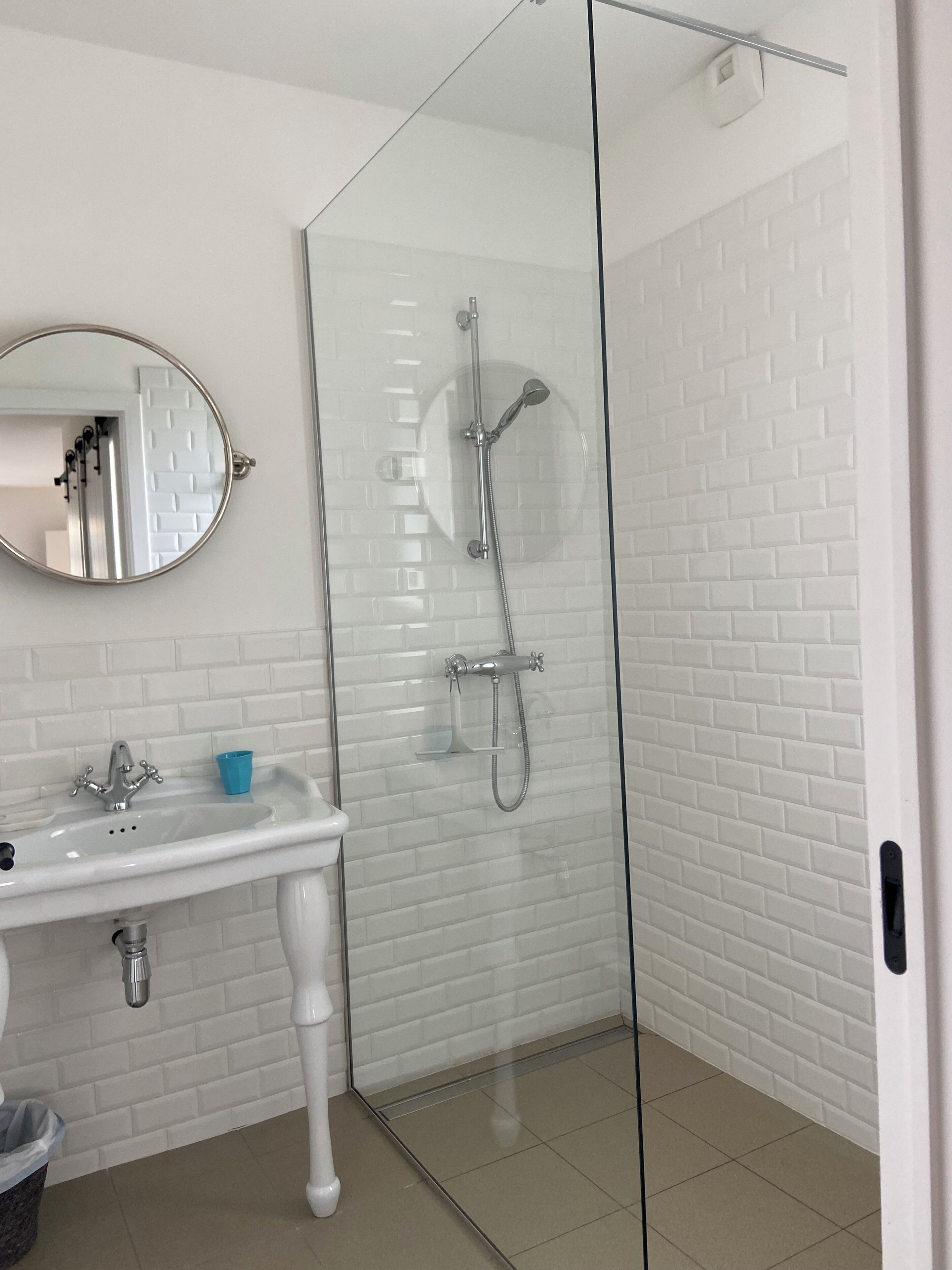 Une salle de bain avec un lavabo blanc, un miroir et une douche fermée par des parois de verre.