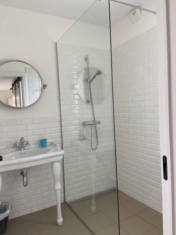 Un baño con lavamanos blanco, espejo y ducha con mampara de vidrio.