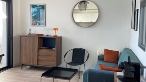 A modern living room with a wooden cabinet, a black chair, a blue sofa, a round mirror, and a hanging light fixture.