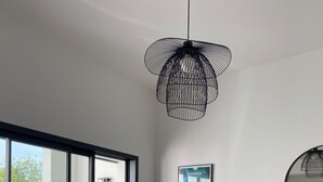 A modern living room with a dining table, a coffee table, a wicker chair, a cabinet, and a hanging light fixture.