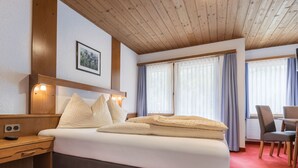Habitación de hotel con cama, mesita de noche, lámpara y vistas al exterior por la ventana.