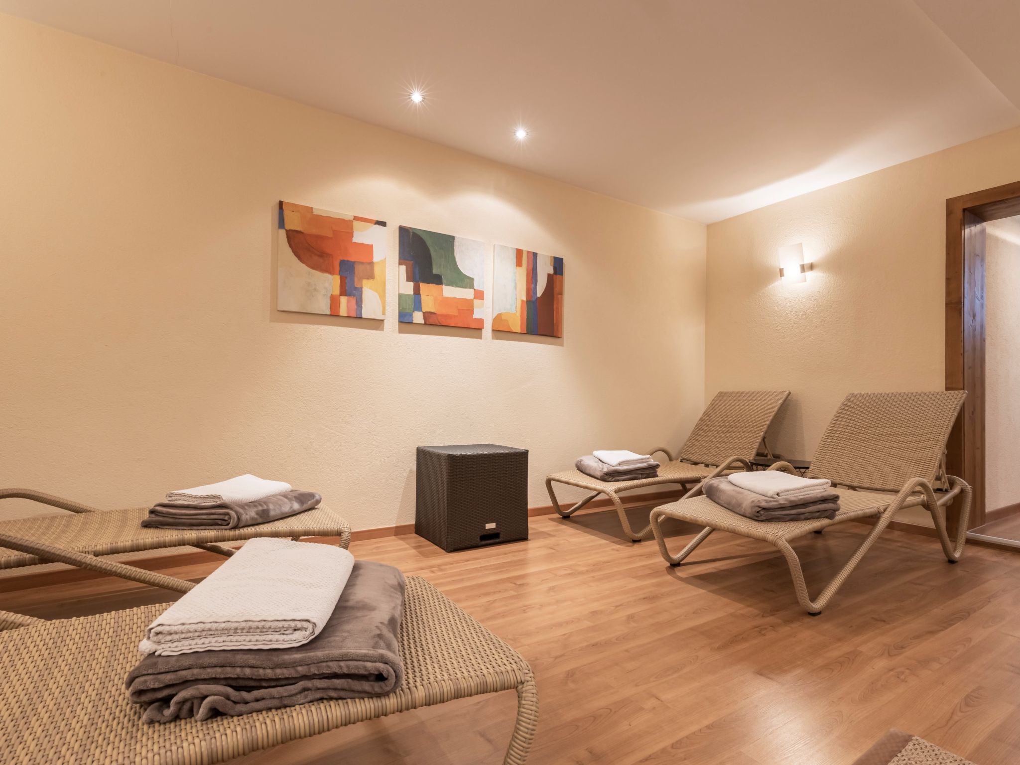 A room with three wicker lounge chairs, a small black speaker, and abstract wall art.