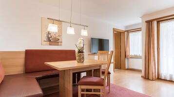 Ein modernes Hotelzimmer mit einem Holztisch, rot gepolsterten Sitzmöglichkeiten, einem Flachbildfernseher und einem großen Fenster mit Vorhängen.