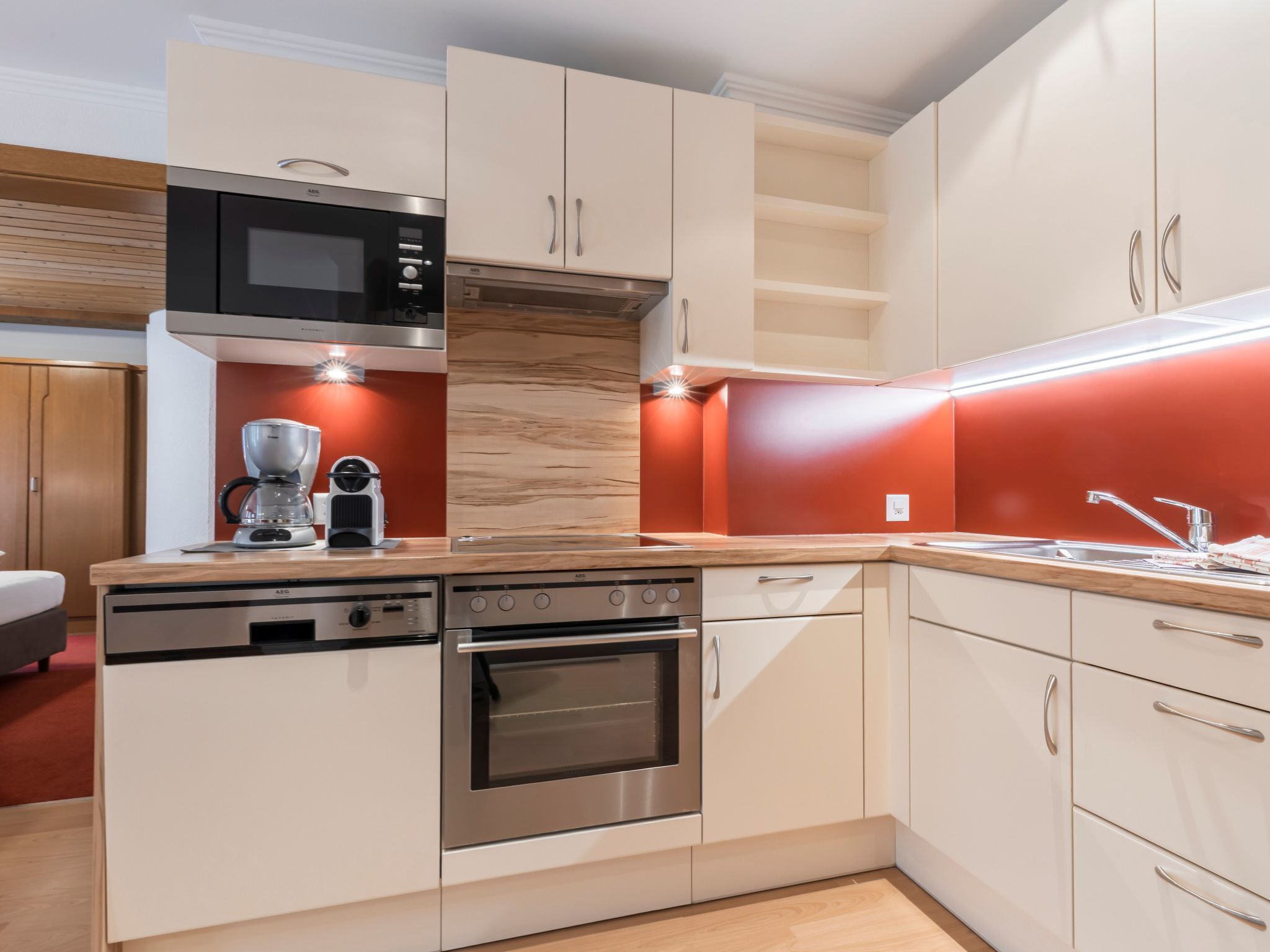 Une cuisine moderne dotée d’appareils électroménagers en acier inoxydable, de plans de travail en bois et d’un mur d’accent rouge.