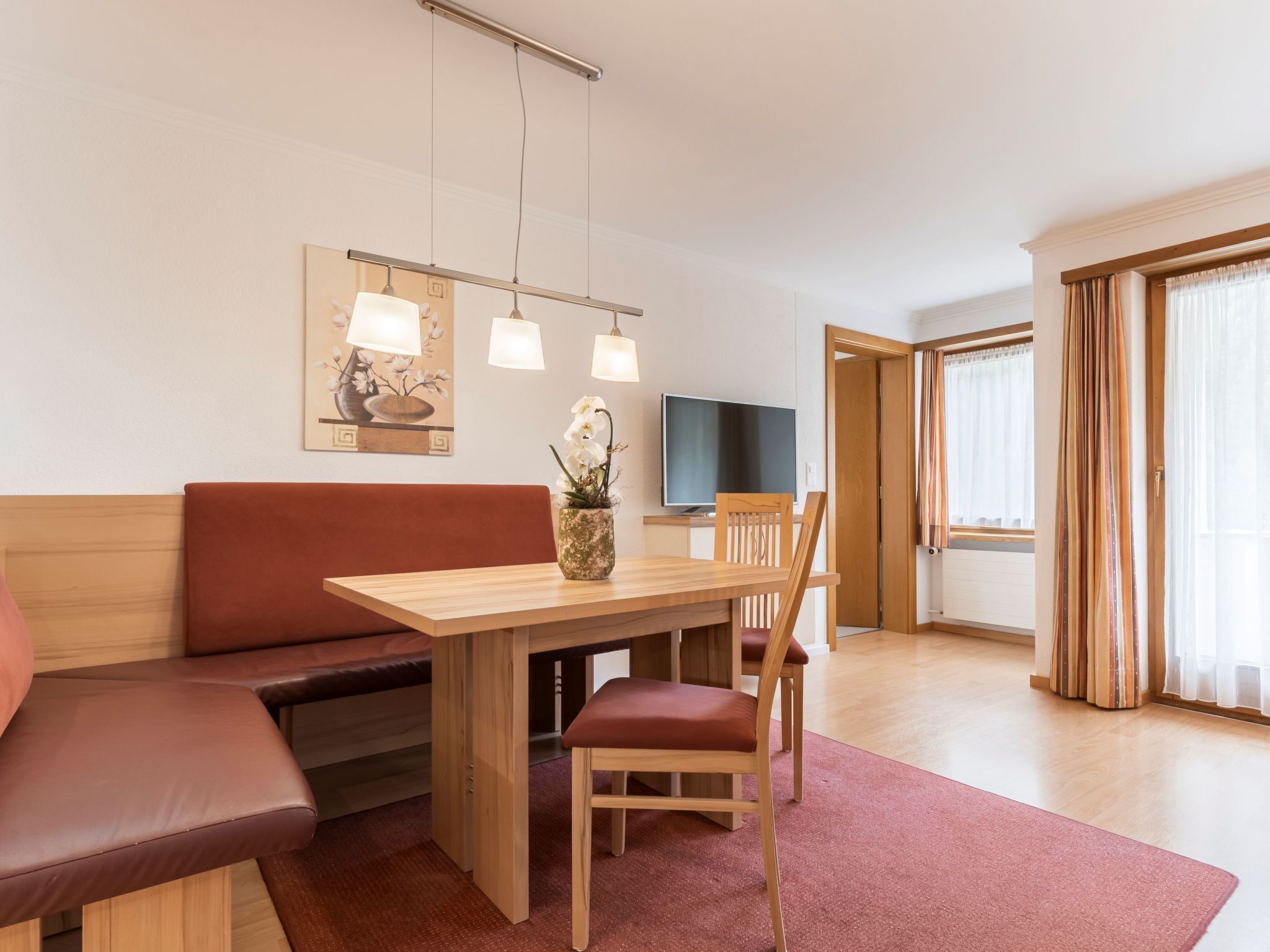 Ein modernes Hotelzimmer mit einem Holztisch, einer Couch, einem Sessel, einem Flachbildfernseher und einem großen Fenster mit Vorhängen.