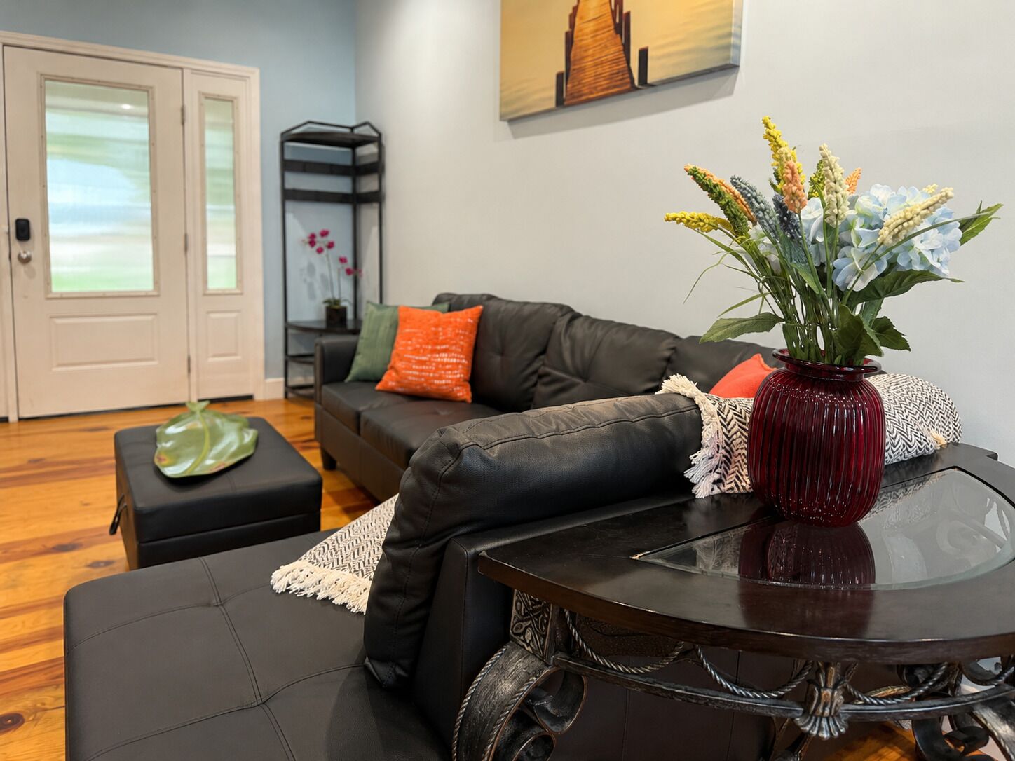 Ein Wohnzimmer mit einem schwarzen Ledersofa, einem Glastisch und einer roten Vase mit Blumen.