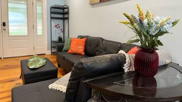 Ein Wohnzimmer mit einem schwarzen Ledersofa, einem Glastisch und einer roten Vase mit Blumen.
