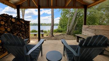 An outdoor seating area with Adirondack chairs and a small round table, overlooking a lake.
