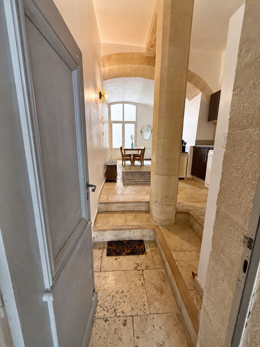 Un couloir menant à une salle à manger équipée d’une table et de chaises, d’une fenêtre et d’une porte.