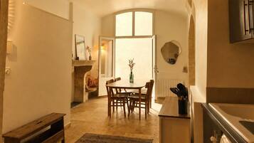 A dining area with a table and chairs, a fireplace, and a view through an open door.