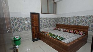 A bedroom with a bed, a ceiling fan, a green trash bin, and a door with a window. - Sehrawat Guest House (Sakrai)