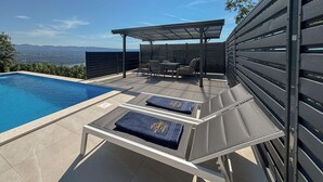 A poolside area with lounge chairs, a covered seating area, and a view of the landscape. - Gorgeous home in Veprinac (Veprinac)